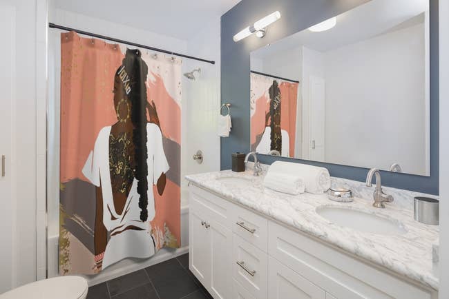 In a bathroom a shower curtain with the design of a woman from behind is shown
