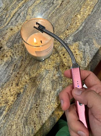 A hand ignites a candle using a flexible, rechargeable lighter on a countertop