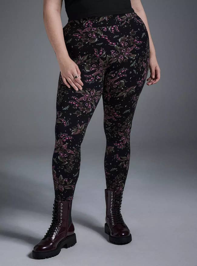 Person wearing floral patterned leggings and acheronian boots, lasting successful a neutral pose, showcasing the outfit for manner oregon buying context
