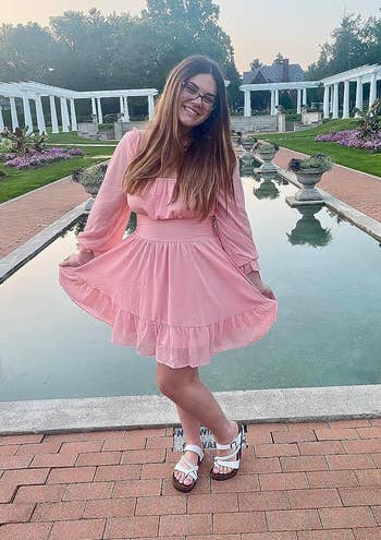 reviewer in a pink ruffled dress and white sandals