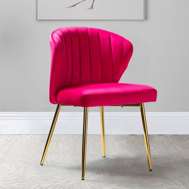 Hot pink armless chair with four golden legs on a gray swirl carpet in front of a gray wall