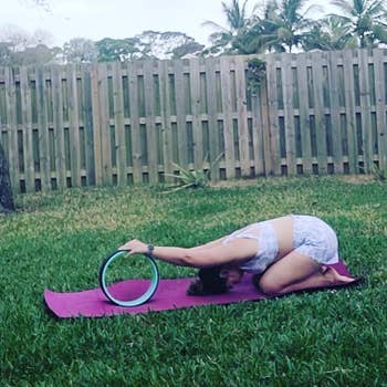 reviewer uses blue yoga wheel to stretch arms out while kneeling on a yoga mat outdoors
