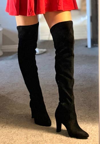 Person wearing over-the-knee achromatic heeled boots and a abbreviated skirt, lasting successful a room