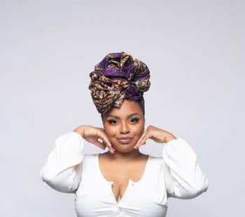 model in white top and patterned headwrap posing with hands on cheeks