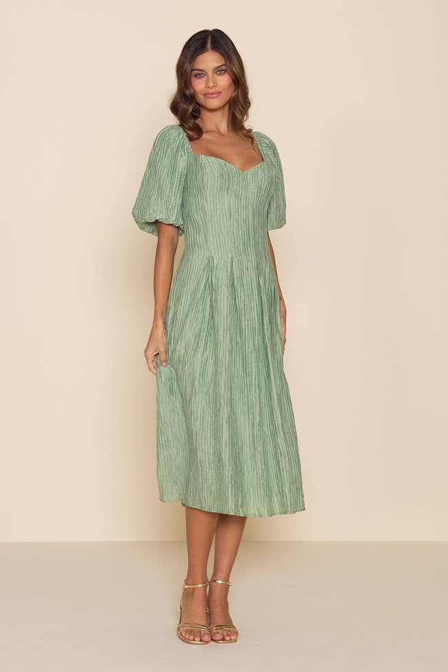 Woman wearing an elegant, pleated, short-sleeved dress with a sweetheart neckline, suitable for a formal event or fashionable outing