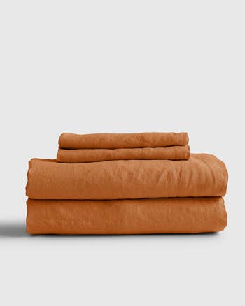 Folded terracotta bedding set including fitted sheet, flat sheet, and pillowcases