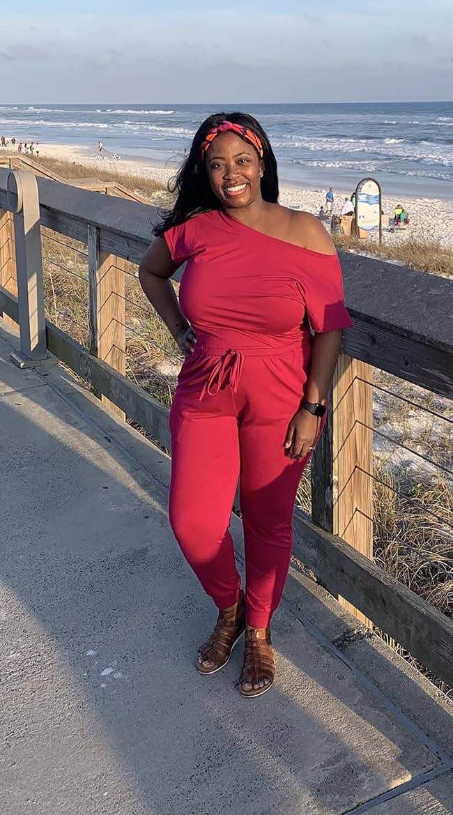 reviewer wearing the short sleeved jumpsuit with a waist tie in red  by the beach