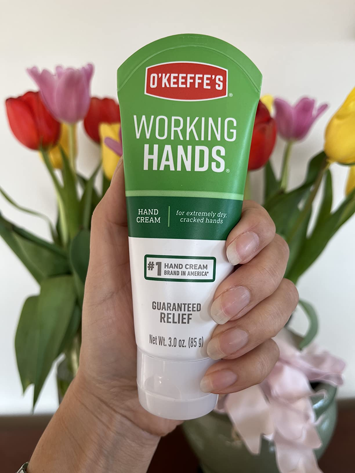 A manus  holding a conduit  of O'Keeffe's Working Hands manus  cream, with colorful flowers successful  the background