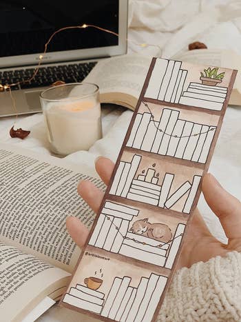 hand holding the blank bookmark illustrated with books on shelves with plants and a cat
