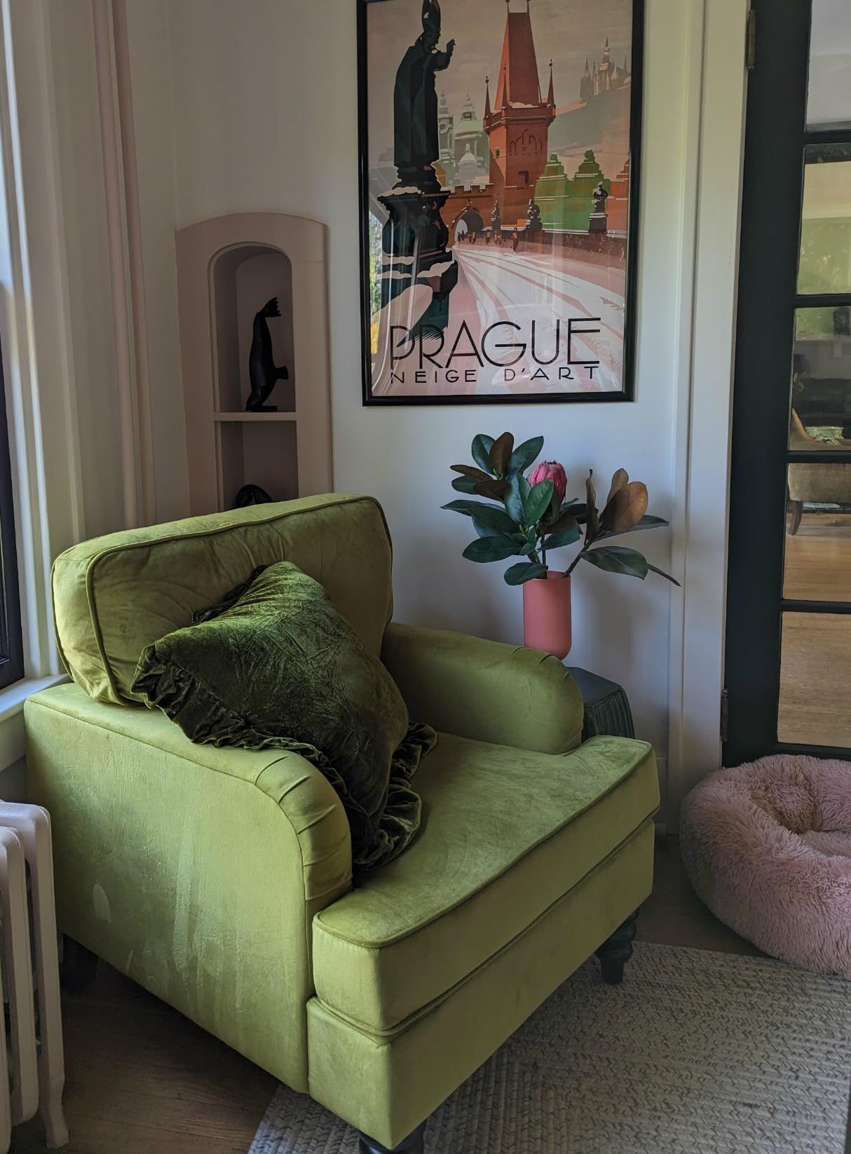 Lengan beludru hijau dengan bantal di kamar yang nyaman, di sebelah poster Praha berbingkai