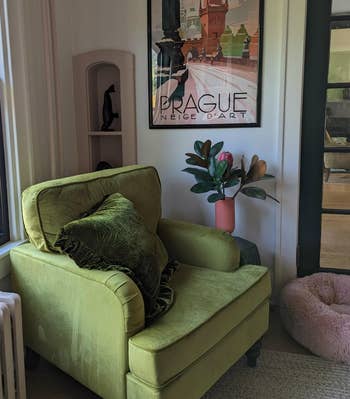 Green velvet armchair with a cushion in a cozy room, next to a framed Prague poster