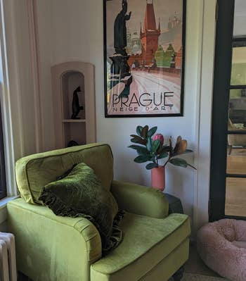 Lengan beludru hijau dengan bantal di kamar yang nyaman, di sebelah poster Praha berbingkai