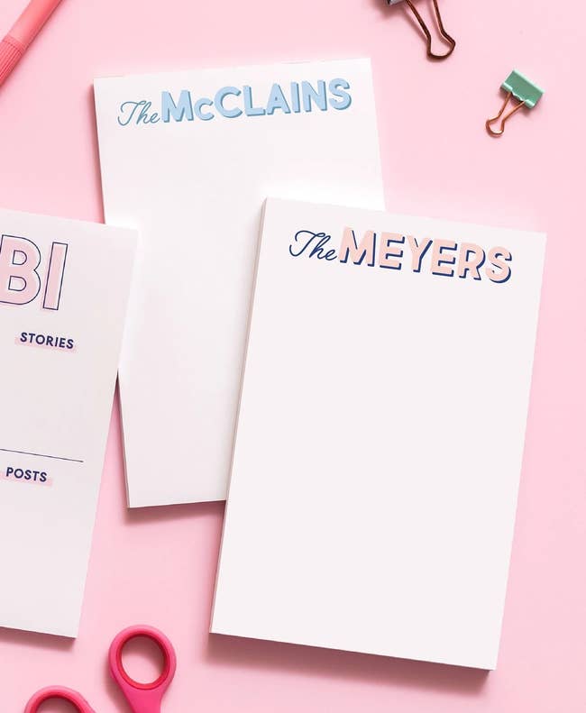 two customized notepads surrounded by office supplies on a pink background