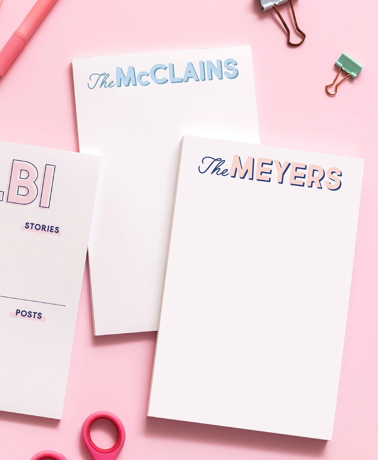 two customized notepads surrounded by office supplies on a pink background