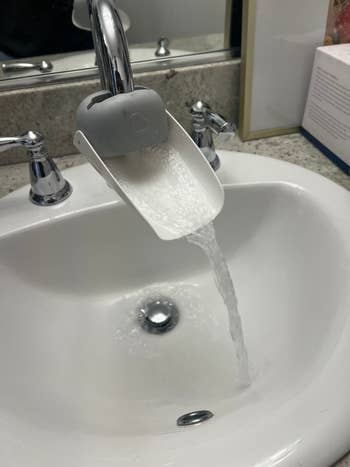 Water flows from a faucet through a white tap attachment into a sink, demonstrating the attachment's function
