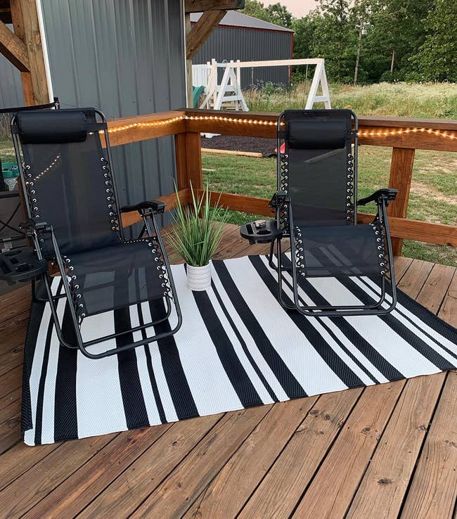 reviewer's two patio chairs placed on a striped mat outdoors near a building with railing and lights