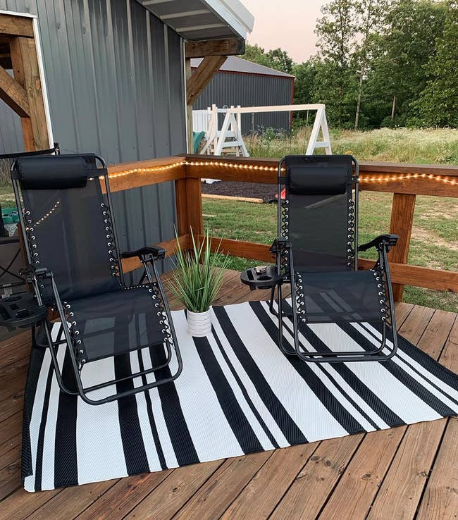 reviewer's 2 patio chairs placed connected a striped mat outdoors adjacent a gathering with railing and lights