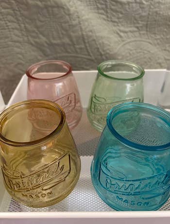 Four mason jar drinking glasses in assorted colors (yellow, pink, green, and blue) displayed on a white tray