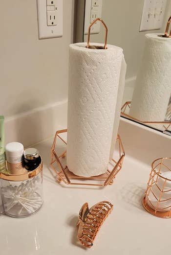 A rose gold geode-shaped wired paper towel holder in a bathroom 