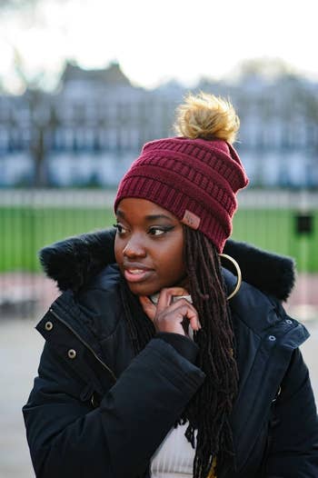 a close up of the red cable knit beanie and brown pom pom