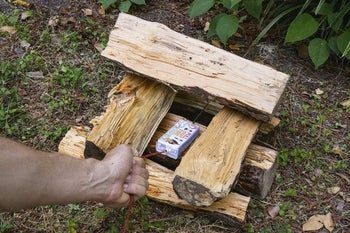 a hand pulling a string on the fire start box, which is sitting on a bed of wood