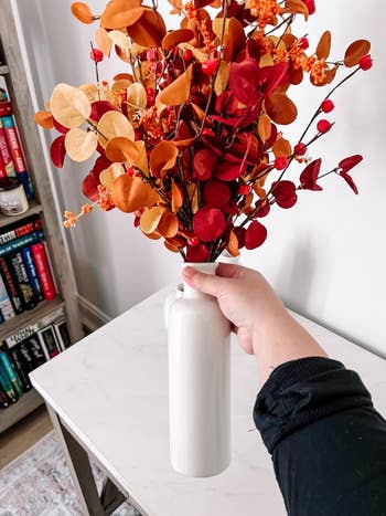 a hand holding up the eucalyptus stems in a white vase