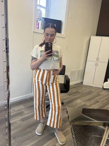 Person successful  a reflector  selfie wearing a cropped graphic tee and striped wide-leg pants. Standing successful  a casual setting
