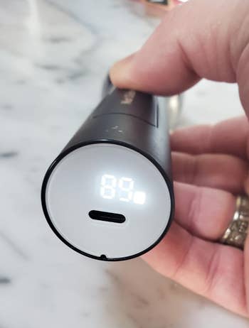 Hand holding a sleek, cylindrical digital thermometer showing a reading of 69 degrees Fahrenheit