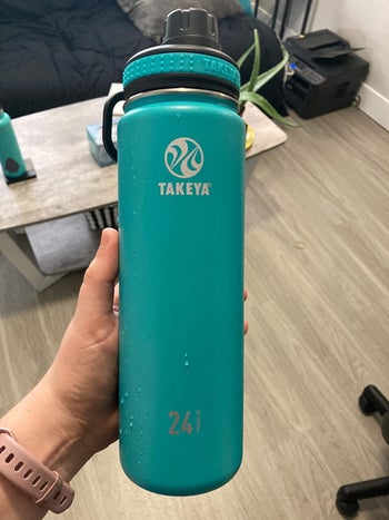 reviewer holding up the turquoise colored takeya bottle