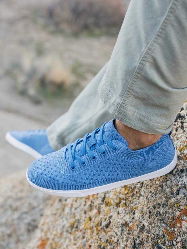 Person wearing blue textured sneakers while standing on a rock, suitable for a shopping category