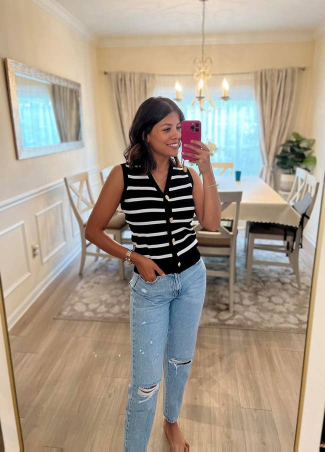 A reviewer wearing a achromatic  and achromatic  striped sleeveless apical  and ripped jeans poses for a reflector  selfie