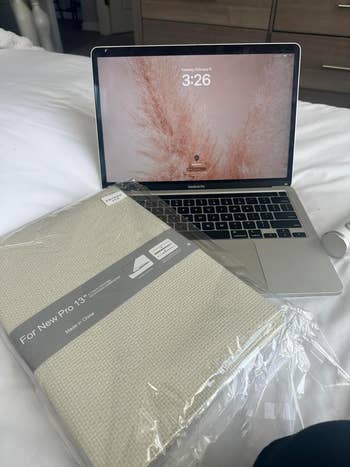 MacBook Pro on bed next to a packaged laptop case for a 13