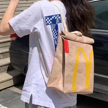 Person in white tee with a tote bag styled after a McDonald's takeout bag
