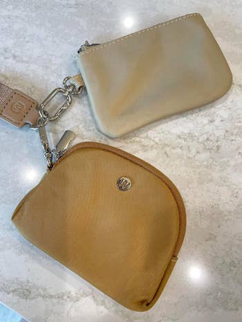 Two tiny  pouch bags with minimalist designs are displayed connected  a marble surface, attached to a keychain with a branded tag
