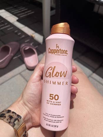 Reviewer holding pink spray bottle of sunscreen 
