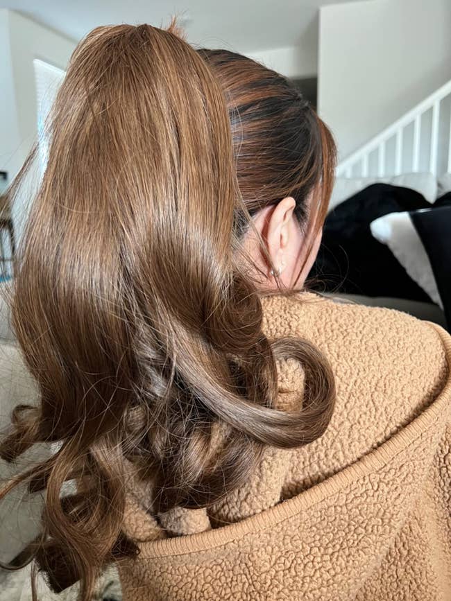 person with long, wavy ponytail wearing a cozy textured jacket, seen from behind, indoors