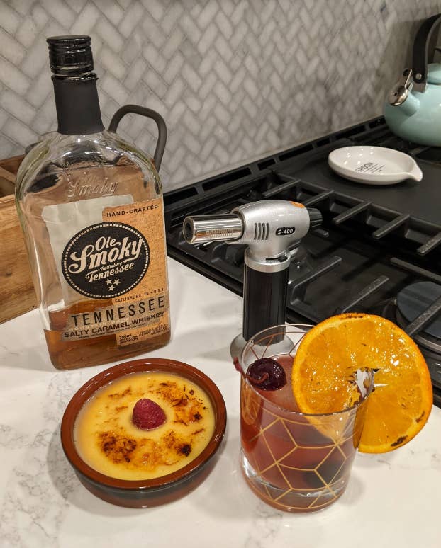 reviewer with torch beside creme brulee and drink with toasted orange