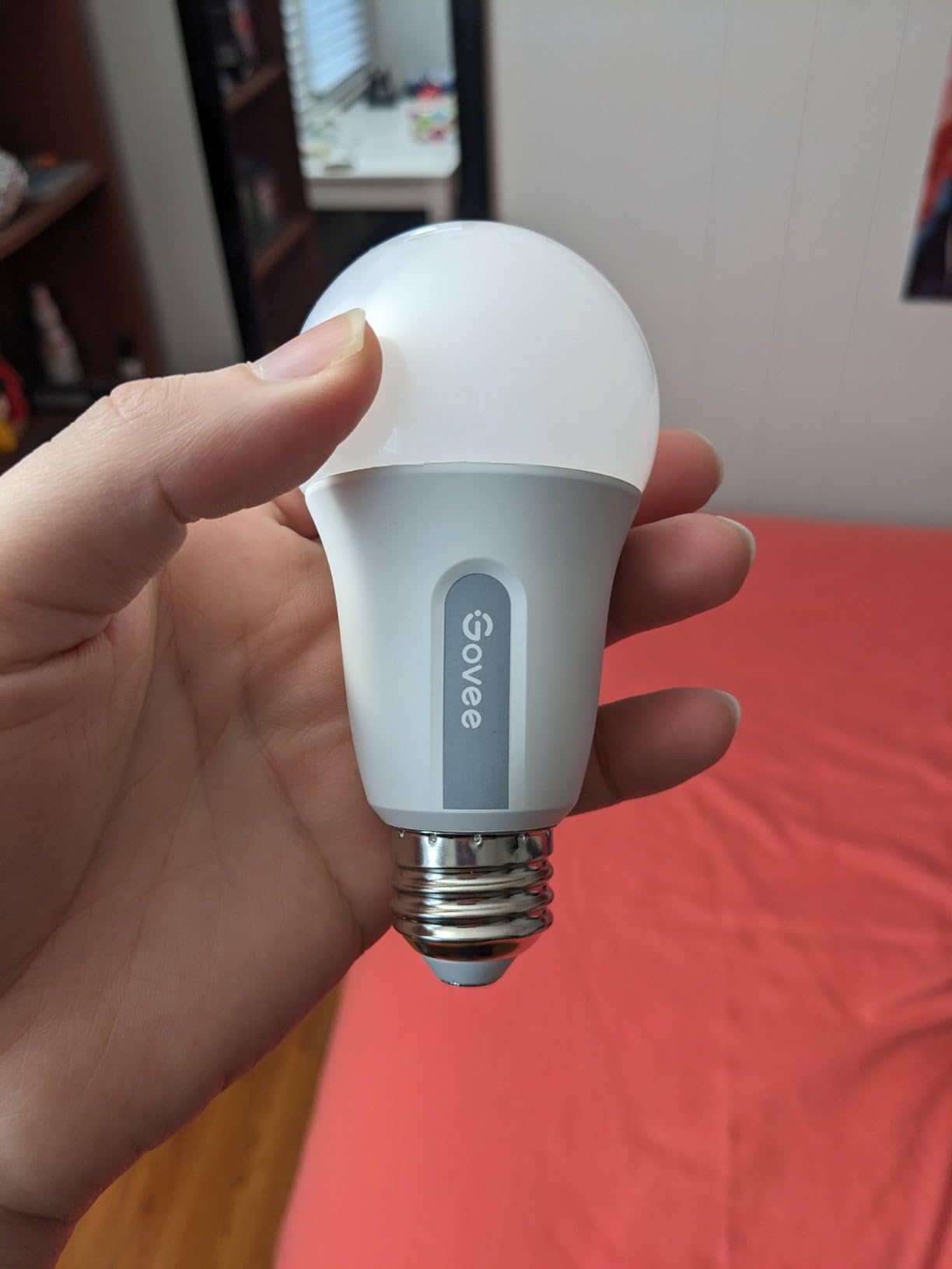 A manus  holding a Govee astute  LED airy  bulb successful  a country   with a pinkish  bedspread successful  the background