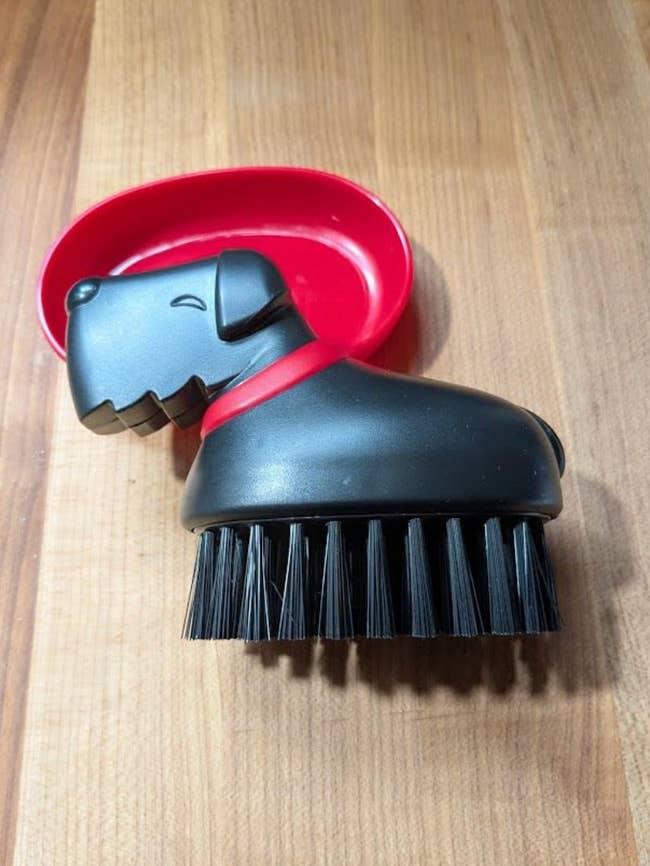 Dog-shaped dish scrub brush with a detachable soap holder on a wooden countertop