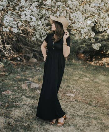 Woman successful a wide-brimmed chapeau and agelong achromatic formal stands successful beforehand of flowering tree, looking to the side. She is outdoors successful a earthy setting