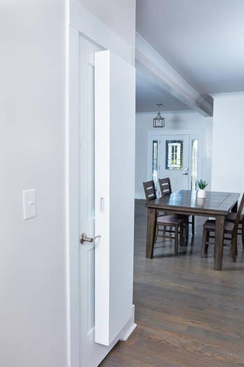 Open white door leading to a dining room with a wooden table and chairs