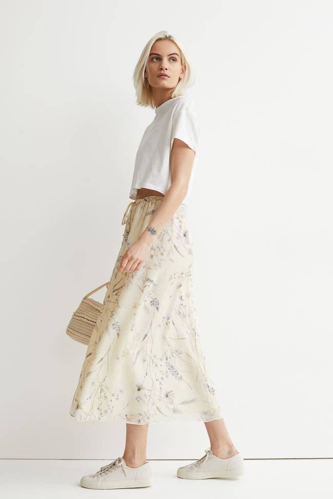 Model is wearing a cream midi skirt with dainty floral designs throughout and a white top