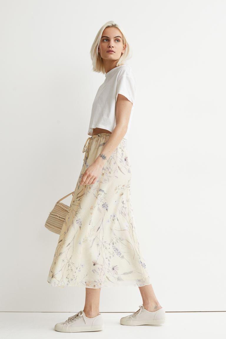 Model is wearing a cream midi skirt with dainty floral designs throughout and a white top