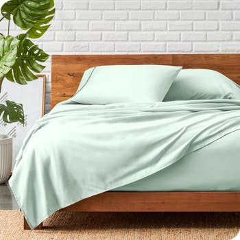Wooden bed frame with mint green bedding, including pillows and duvet, in a room with a potted plant