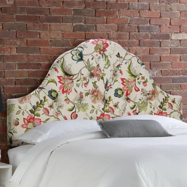 Cream rounded tufted headboard with pink, blue, and green floral pattern attached to a bed against a brick wall