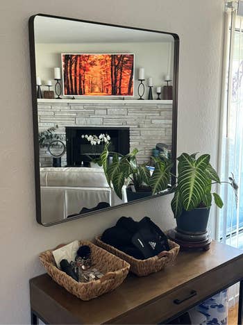 A modern living room reflected in a mirror above a console table with decorative plants and baskets