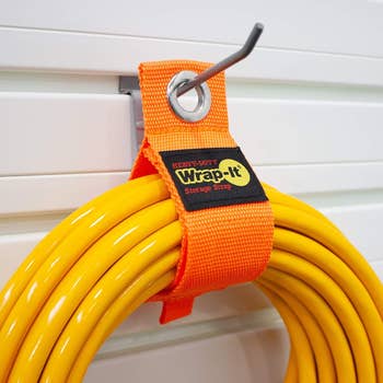 Heavy-duty Wrap-It storage strap holds a coiled yellow hose on a metal hook attached to a wall panel