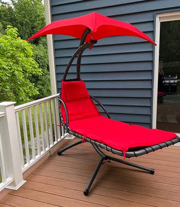 Red hanging chaise lounge chair with canopy on a deck