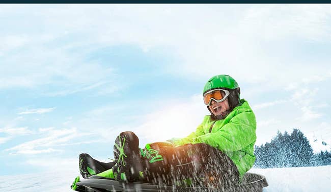 Child model riding green and black snow sled down hill