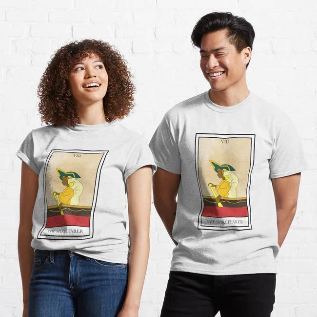 two model swearing white t-shirts with a tarot card design on it of stella and her cat in a boat from spiritfarer